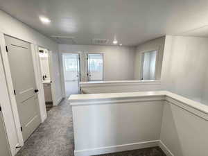 Hall featuring dark colored carpet, an upstairs landing, recessed lighting, and a textured ceiling