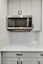 Kitchen view of stainless steel microwave, decorative backsplash, light stone countertops, and white cabinetry