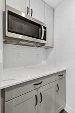 Kitchen view of stainless steel microwave, decorative backsplash, light stone counters, and white cabinetry