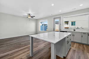 Kitchen with a center island, dark wood-style floors, light stone counters, gray cabinetry, and recessed lighting
