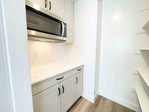 Kitchen with stainless steel microwave, white cabinetry, light stone countertops, light wood-style flooring, and tasteful backsplash
