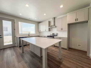 Kitchen featuring a kitchen breakfast bar, wall chimney range hood, dark wood finished floors, stainless steel appliances, and white cabinets