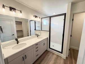 Full bath with a spacious closet, a shower stall, double vanity, dark wood finished floors, and a textured ceiling