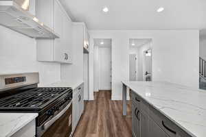Kitchen featuring stainless steel range with gas cooktop, range hood, light stone countertops, dark wood-type flooring, and recessed lighting
