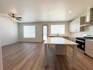 Kitchen with stainless steel gas stove, wall chimney exhaust hood, backsplash, light wood-type flooring, and recessed lighting