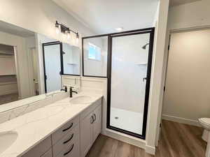 Full bath featuring a stall shower, double vanity, dark wood finished floors, and a spacious closet