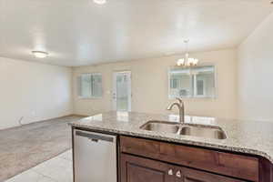Kitchen with light carpet, stainless steel dishwasher, a textured ceiling, light tile patterned floors, and hanging light fixtures