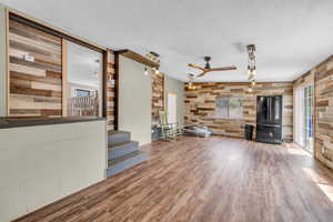 Unfurnished living room featuring wood walls, ceiling fan, wood finished floors, a textured ceiling, and stairs