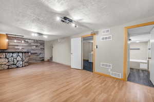 Basement with wooden walls, light wood-type flooring, a textured ceiling, an accent wall, and washer / clothes dryer