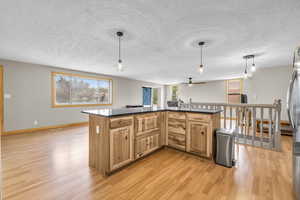 Kitchen featuring dark countertops, a textured ceiling, a kitchen island, light wood-style flooring, and decorative light fixtures