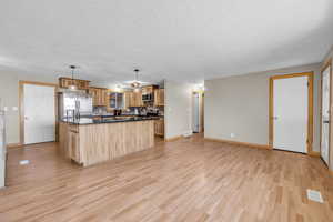 Kitchen with a center island, light wood-type flooring, stainless steel appliances, tasteful backsplash, and a textured ceiling