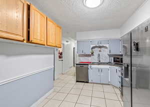 Kitchen with appliances with stainless steel finishes, backsplash, light tile patterned floors, a textured ceiling, and dark stone countertops