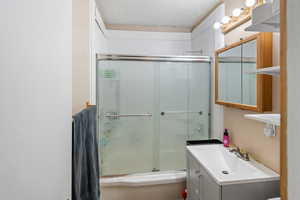 Bathroom featuring enclosed tub / shower combo, vanity, and a textured ceiling