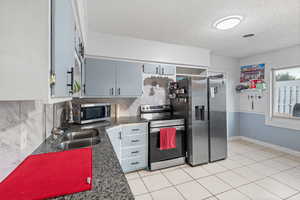 Kitchen featuring stainless steel appliances, tasteful backsplash, light tile patterned floors, and a textured ceiling