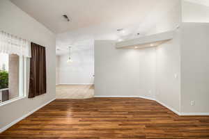 Spare room featuring dark wood-type flooring, hanging lights, and vaulted ceiling