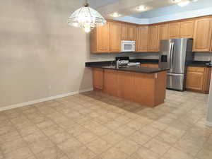 Kitchen with white appliances, a peninsula, a chandelier, hanging light fixtures, and brown cabinets