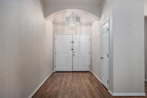 Foyer entrance featuring arched walkways, dark wood-style floors, and suspended lighting