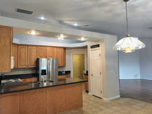 Kitchen with stainless steel fridge with ice dispenser, a peninsula, brown cabinetry, a chandelier, and electric range oven
