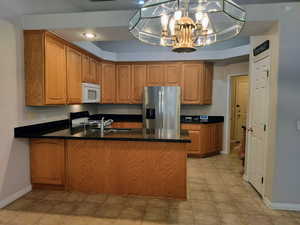 Kitchen featuring a peninsula, stainless steel fridge, brown cabinetry, dark counters, and white microwave