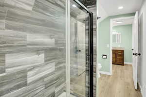 Bathroom with a stall shower, light wood finished floors, and vaulted ceiling