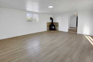 Unfurnished living room with a wood stove, light wood finished floors, and a textured ceiling