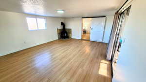 Unfurnished bedroom with a wood stove, a textured ceiling, and light wood-style flooring