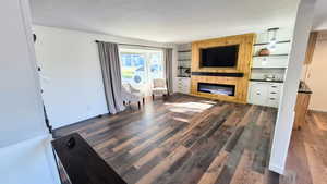 Unfurnished living room featuring a glass covered fireplace, built in shelves, dark wood-type flooring, and a textured ceiling
