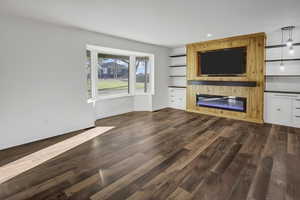 Unfurnished living room with built in features, a glass covered fireplace, dark wood-style flooring, and recessed lighting