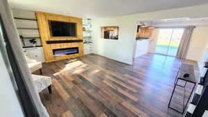 Unfurnished living room featuring a large fireplace, built in features, and dark wood-style flooring