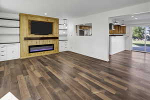 Unfurnished living room with recessed lighting, dark wood-type flooring, built in features, and a glass covered fireplace