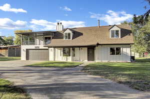 View of front facade with board and batten siding, driveway, a shingled roof, and a chimney