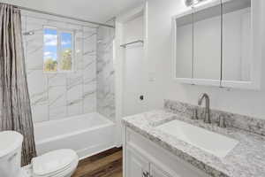 Bathroom featuring shower / bath combination with curtain, vanity, and dark wood-type flooring