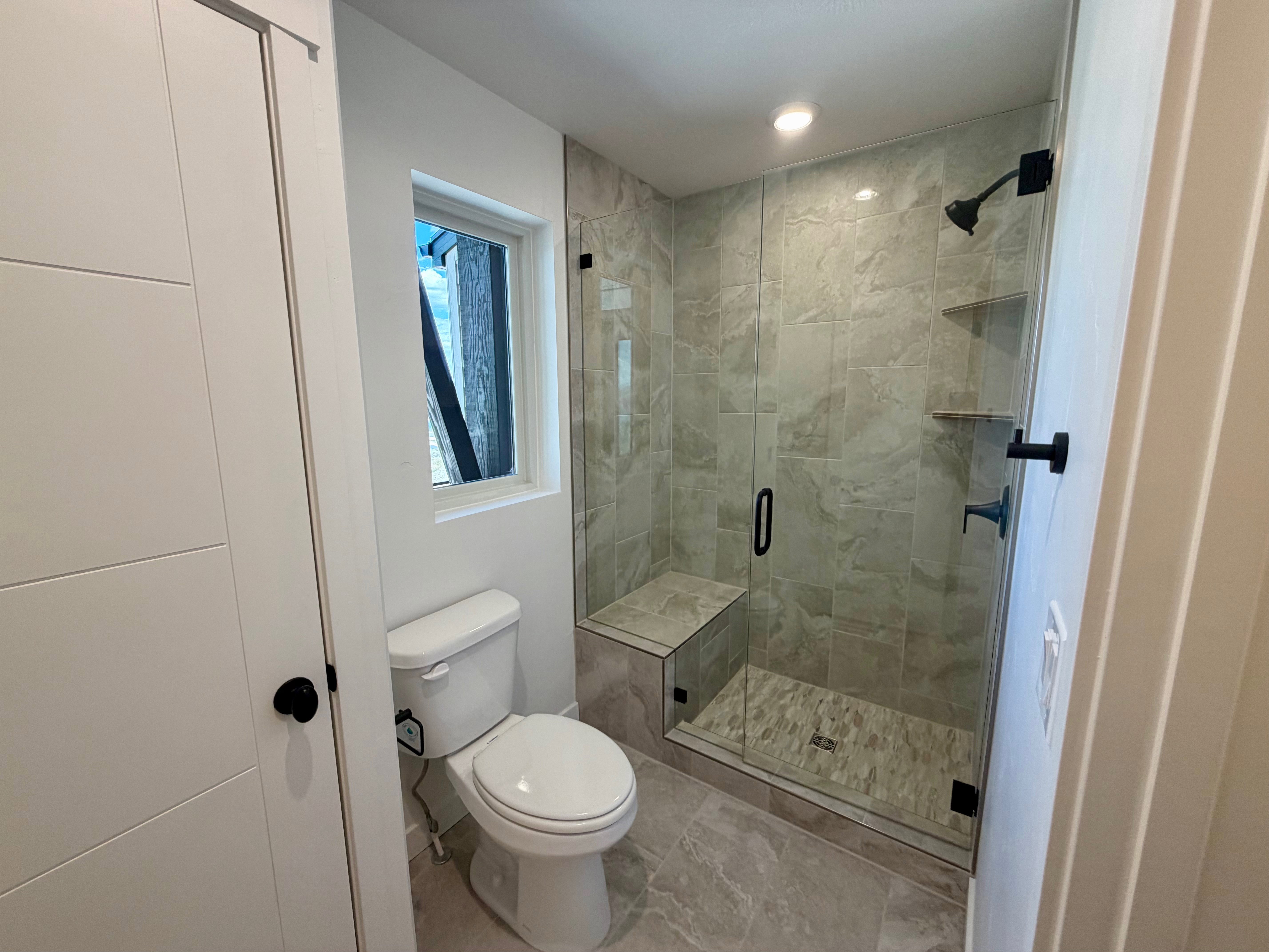Contemporary bathroom featuring a glass-enclosed shower with a built-in bench, a wall-mounted showerhead, and black fixtures