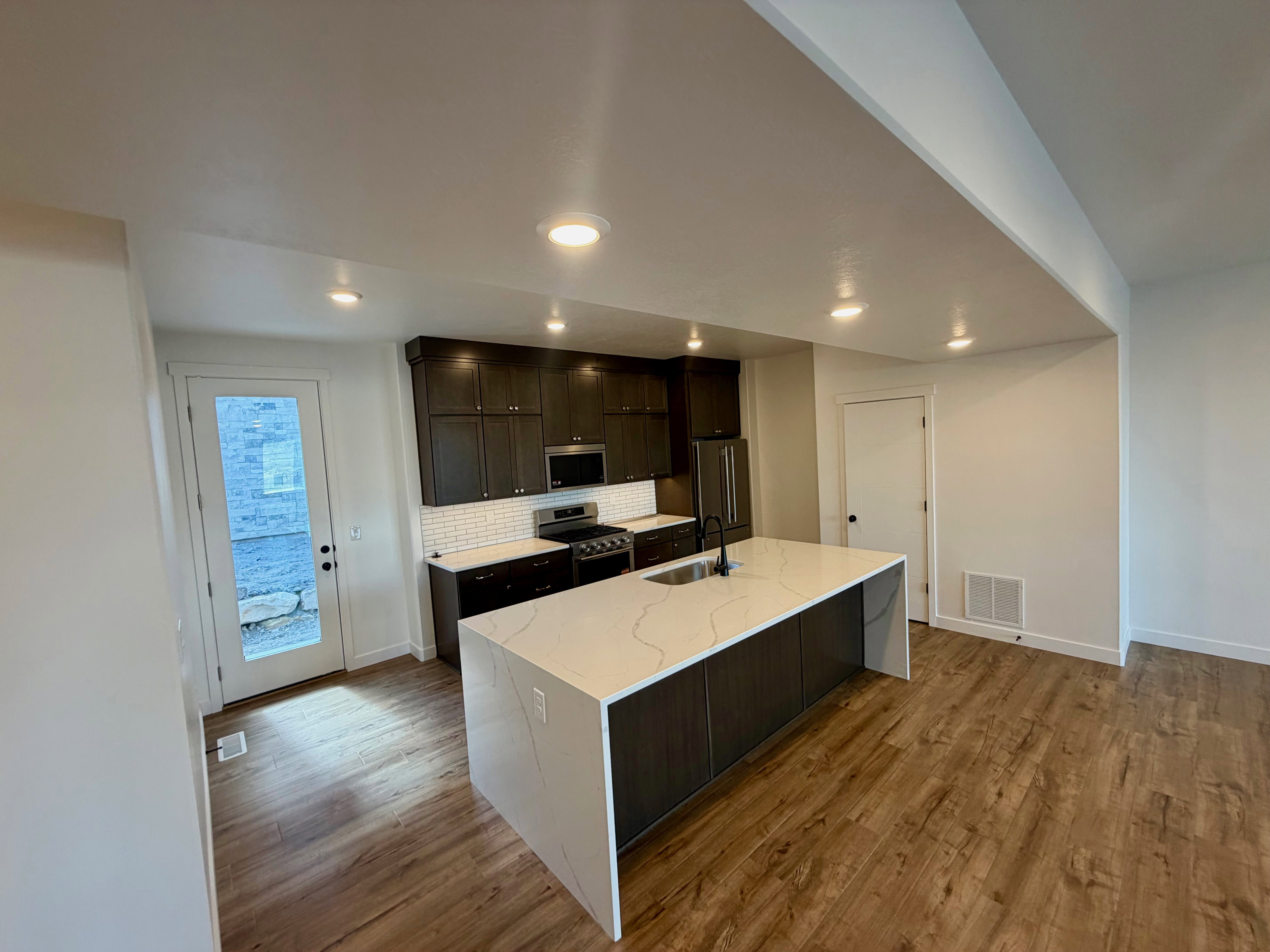 Kitchen featuring a large central island with a waterfall countertop, dark wood-finish cabinetry, stainless steel appliances, and wood-finish flooring