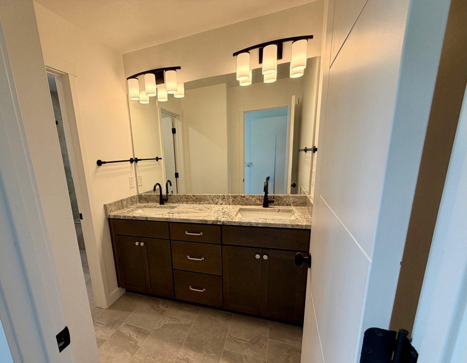 Dual vanity with dark wood-finish cabinetry, granite-style countertops, and matte black fixtures