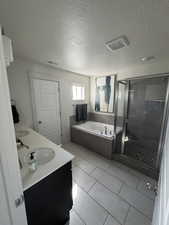 Bathroom featuring a bath, a stall shower, double vanity, light tile patterned floors, and a textured ceiling