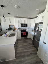 Kitchen featuring hanging light fixtures, a peninsula, white cabinetry, appliances with stainless steel finishes, and light stone countertops