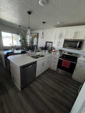 Kitchen featuring a peninsula, appliances with stainless steel finishes, white cabinetry, dark wood-type flooring, and a textured ceiling