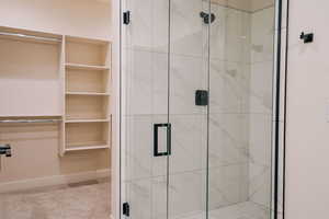 Bathroom featuring a marble finish shower, a spacious closet, and light colored carpet