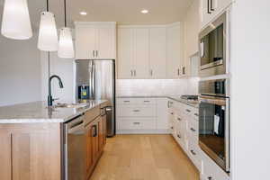 Kitchen with white cabinetry, light stone countertops, stainless steel appliances, decorative backsplash, and decorative light fixtures