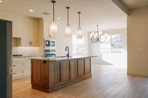 Kitchen with light stone counters, decorative backsplash, a kitchen island with sink, appliances with stainless steel finishes, and decorative light fixtures