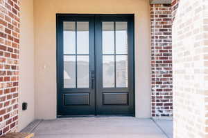 View of exterior entry with brick siding, french doors, and stucco siding
