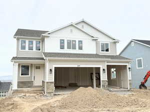 View of front facade featuring roof with shingles, an attached garage, stone siding, and covered porch