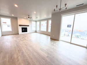 Unfurnished living room featuring a textured ceiling, a fireplace, plenty of natural light, ceiling fan, and light wood-style floors