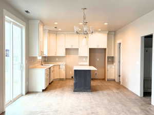 Kitchen with white cabinets, hanging light fixtures, a center island, a chandelier, and recessed lighting