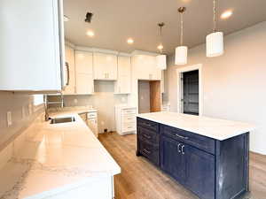 Kitchen featuring a center island, light wood finished floors, light stone counters, hanging light fixtures, and white cabinetry