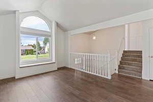 Unfurnished living room featuring dark wood-type flooring, vaulted ceiling, and stairs