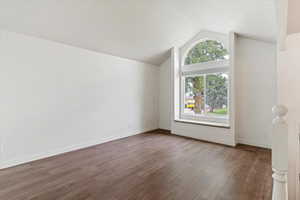 Additional living space with dark wood-style flooring and vaulted ceiling