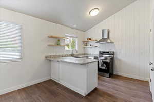Kitchen with electric range, wall chimney range hood, a peninsula, light stone countertops, and dark wood-style floors