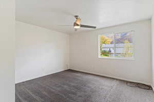 Empty room featuring dark carpet, a textured ceiling, and ceiling fan